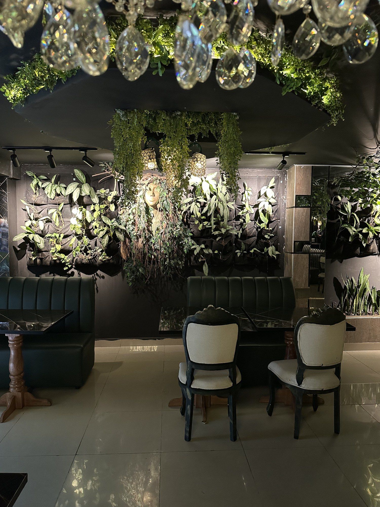 Pared cubierta de plantas con sillas blancas y lámpara de cristal